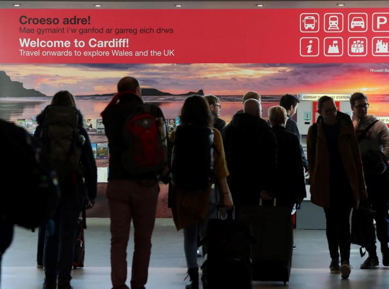 People walking into arrivals at Cardiff airport, with welcome sign on background wall. 