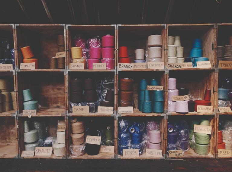 Different colour yarn being stored in compartments on shelves.