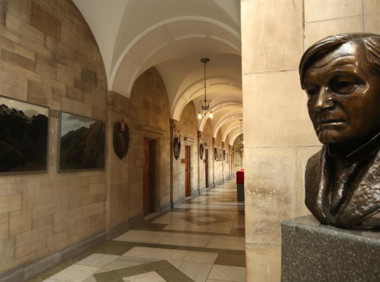 Aspects of Main Arts Building Bangor University with stone walls tiled cream floor and head statue of man in the forefront.