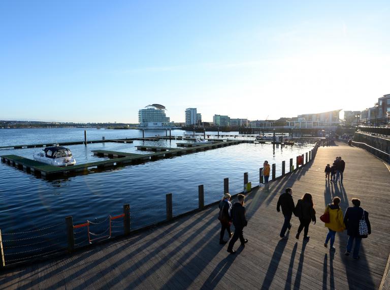 People walking at Cardiff Bay with the St David's Spa Hotel in the distance