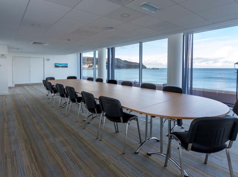Boardroom desk with chairs around looking out of the floor to ceiling windows onto the sea and promenade. 