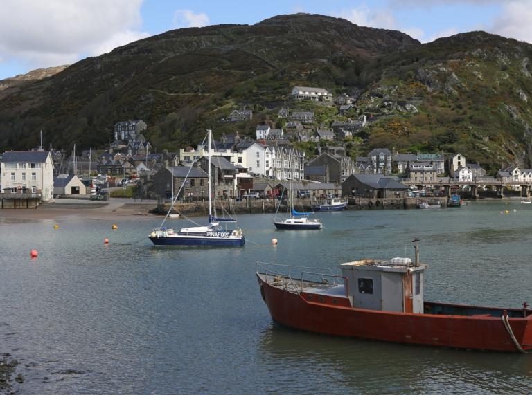 Image of small boats in Barmouth harbor with houses and hills in the background.