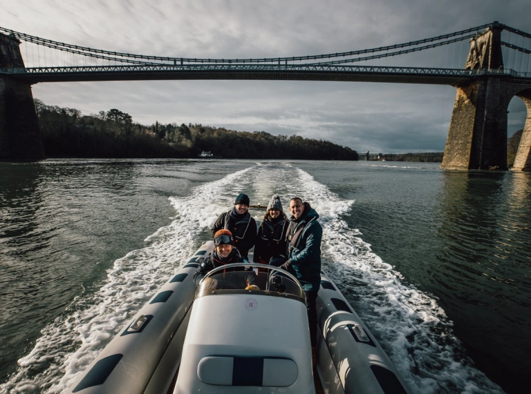 Four people on a boat ride with the Menai Bridge behind them