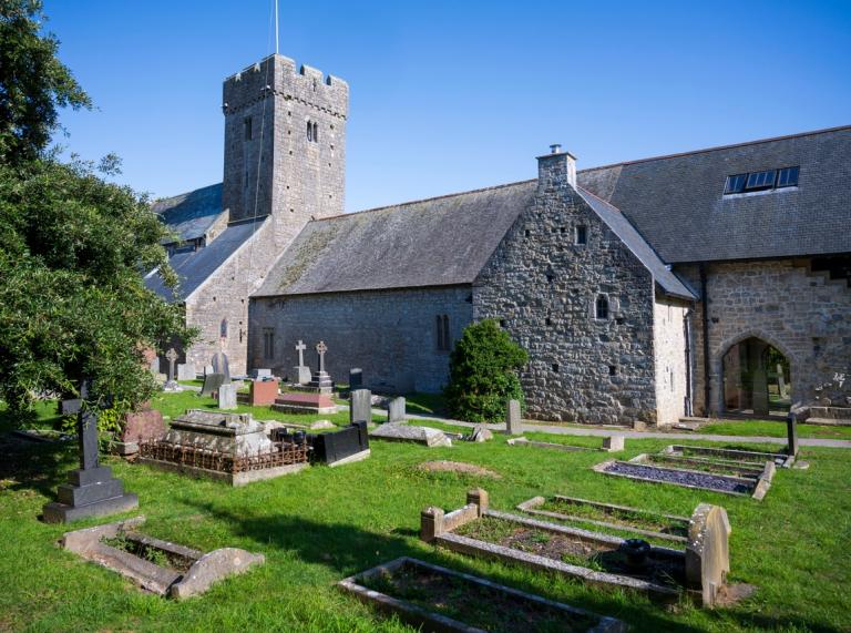 Exterior view of St Illtyd's Church with blue skies and graves outside