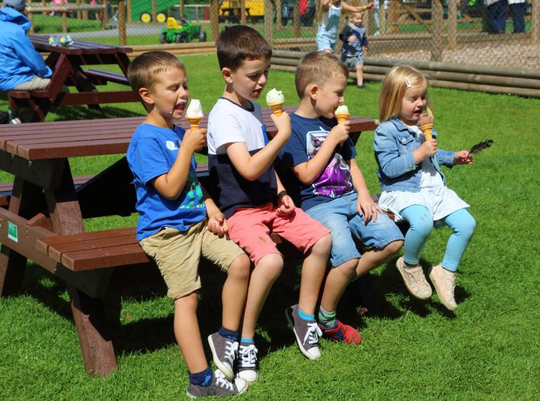 four children sat on bench eating ice cream.