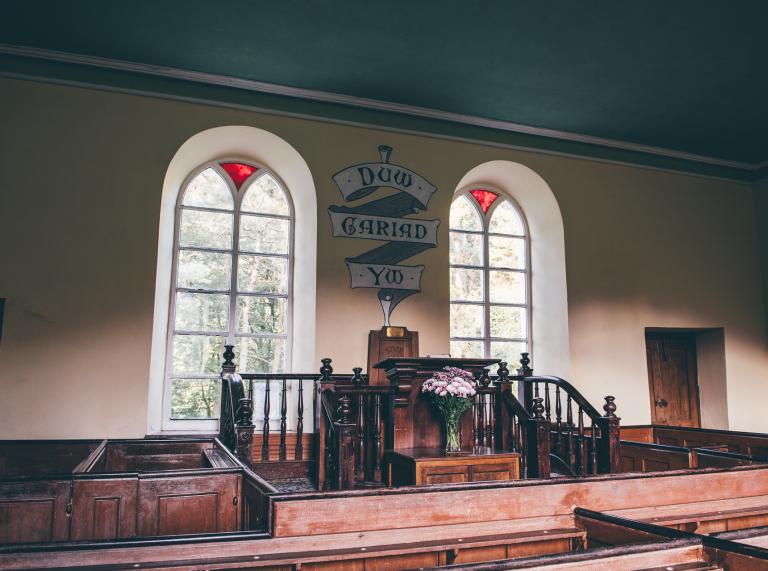 interior of chapel with stained glassed windows, painted sign and altar.