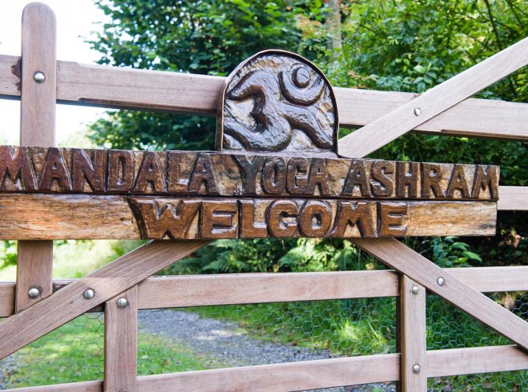 Wooden gate with carved 'Mandala Yoga Ashram Welcome' sign