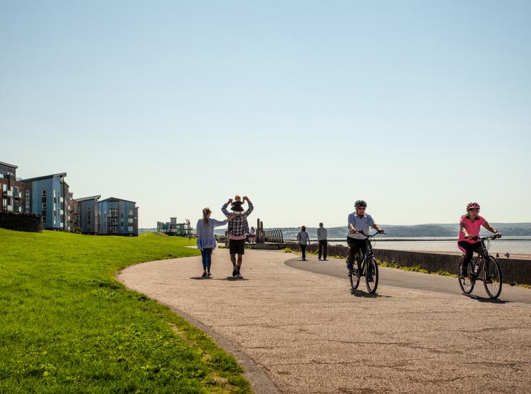Spaziergänger und Radfahrer auf einem breiten Weg am Meer.