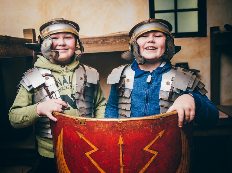 two boys dressed as Roman soldiers holding a shield.