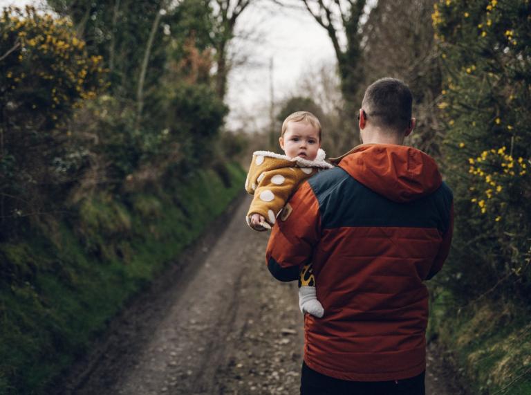A man carrying a baby on a path surrounded by trees 