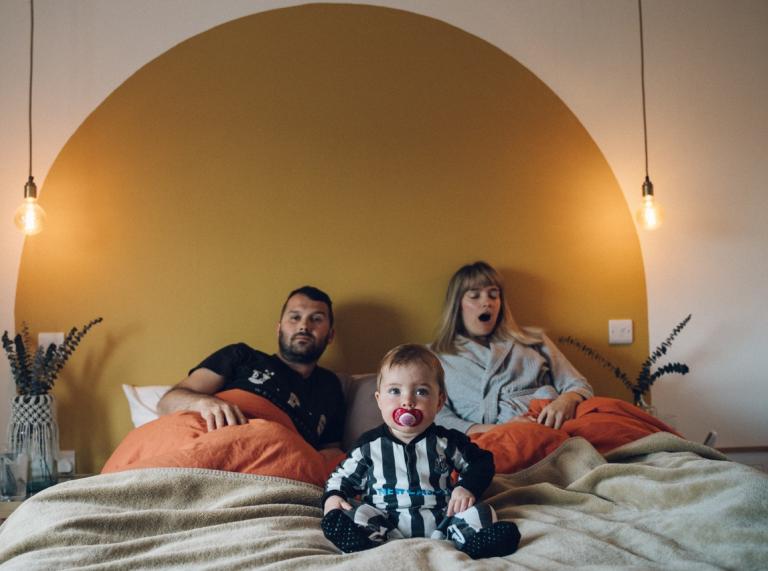 A man, woman and baby sitting up in bed