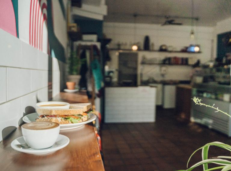 A cup of coffee and a sandwich on a wooden bar inside a café