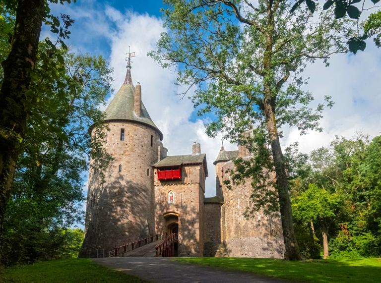 exterior of Castle Coch, the fairy tale style castle, against a blue sky with white cloud and with trees in the foreground
