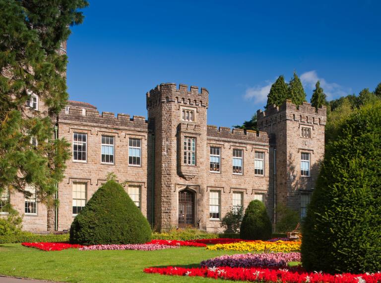 A castle-style building with towers and many windows and a colourful garden.