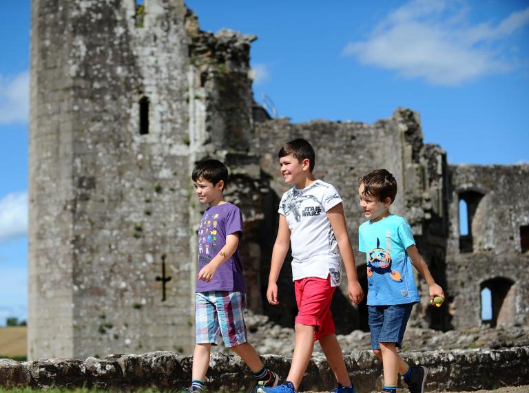 three boys walking with castle walls in background.