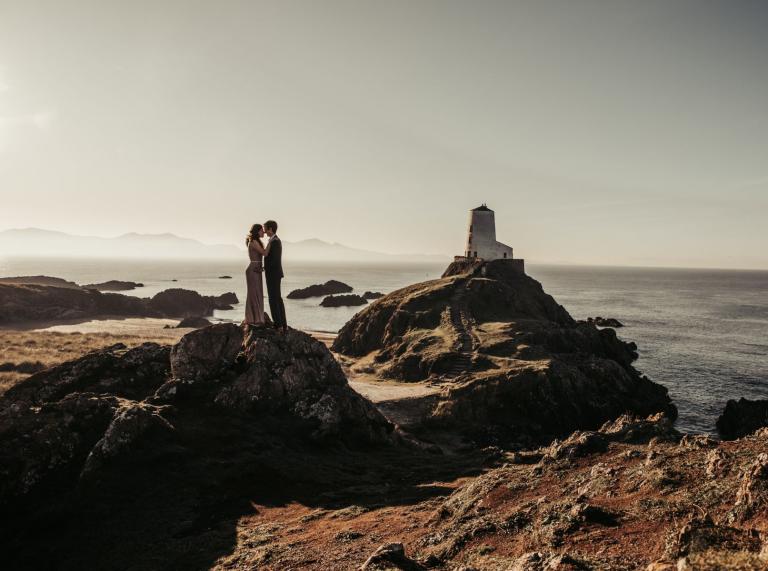 A bride and groom hugging in front of an island with a lighthouse on it.