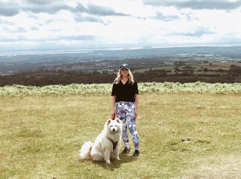 A woman and a white, furry dog on a hillside.