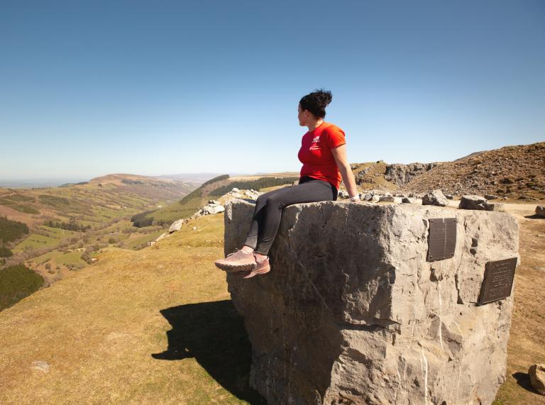 Woman sitting on a large stone looking out across the view.