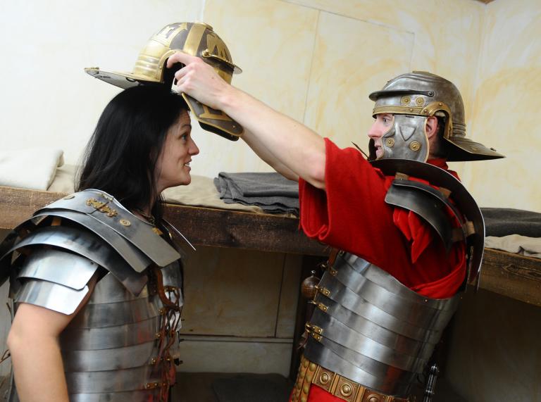 A man dressed as a Roman soldier putting a Roman helmet on a woman.