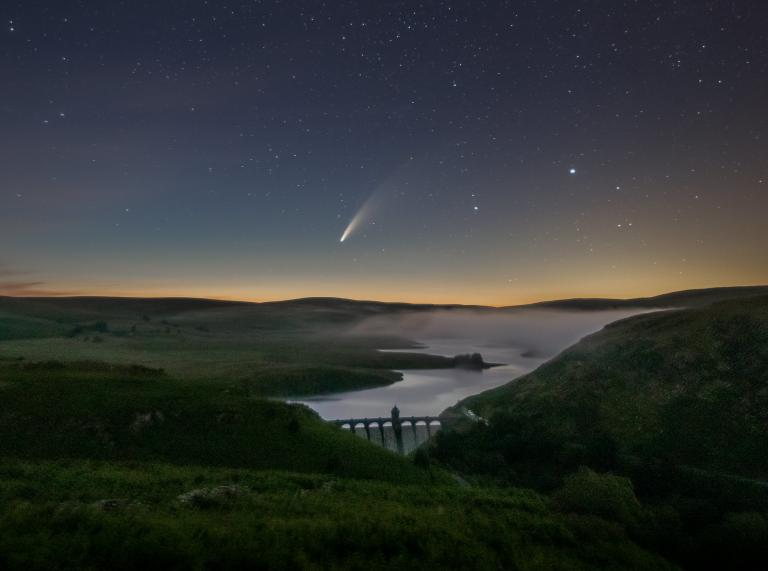 Comet in the night's sky above a dam.