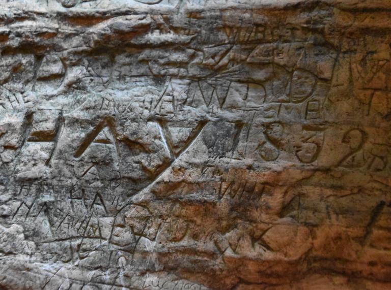 Names and numbers carved out of rock inside a cave.