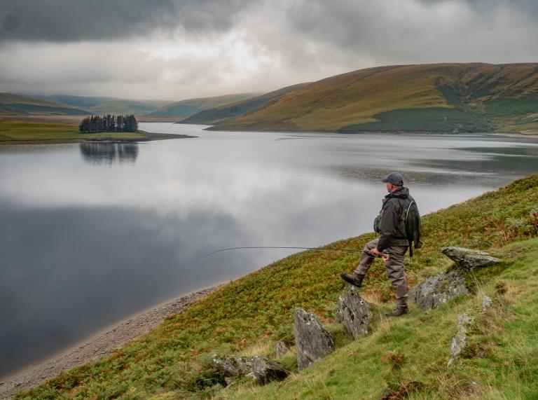A man fishing by a large reservoir.