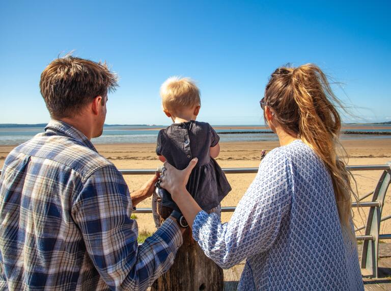 man and woman with toddler looking towards beach.