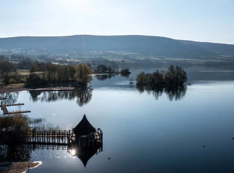 A sparkling lake surrounded by woodland and mountains.