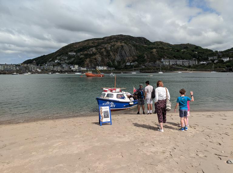 A group of people stood by a small ferry on a sandy beach.