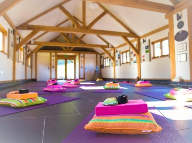 yoga mats and brightly coloured pillows in large room with wooden beams.