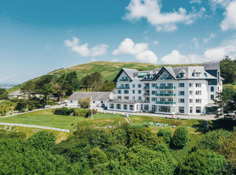 Ein großes, weiß gestrichenes Hotel, umgeben von Rasenflächen und Wäldern.