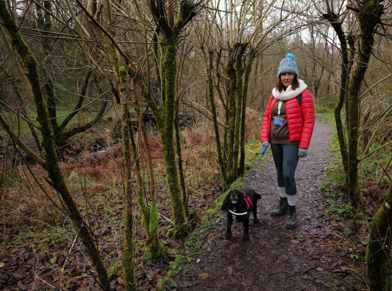 A woman and a dog on a woodland path.