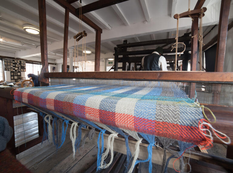 blanket on weaving machine, with man weaving in background.