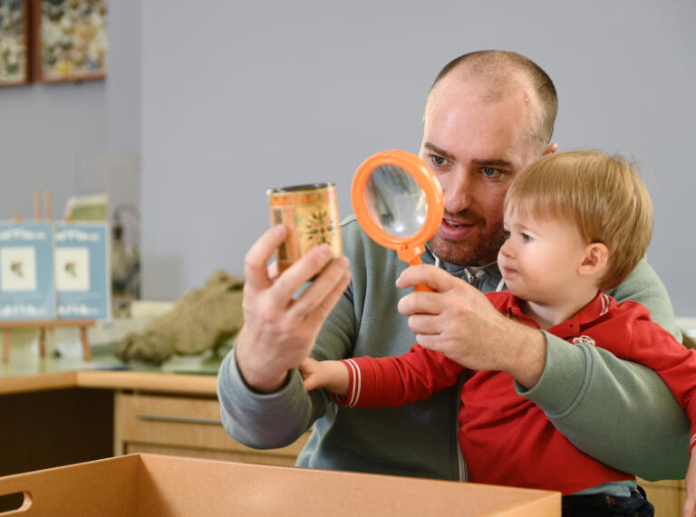 man holding magnifying glass and small object with young boy looking.