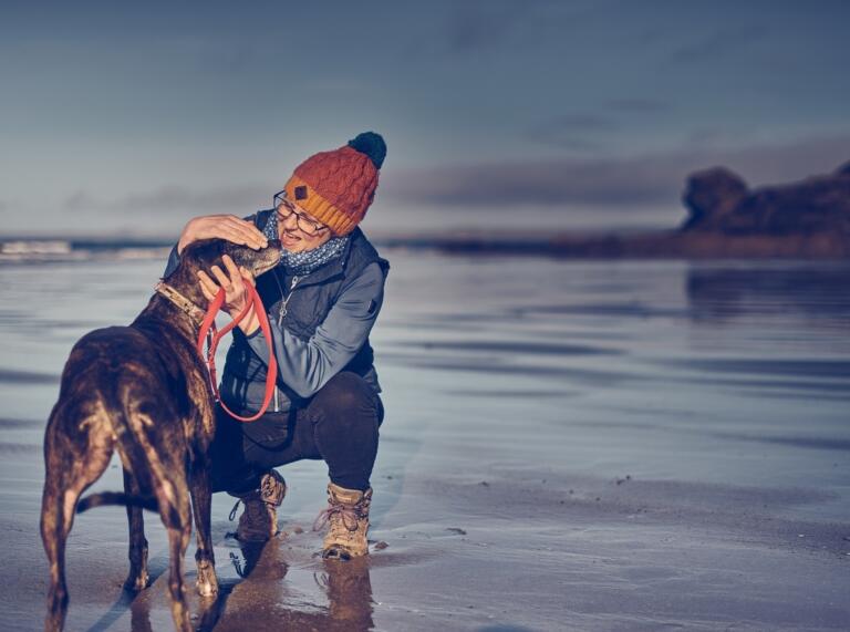 woman crouched stroking dog on beach.