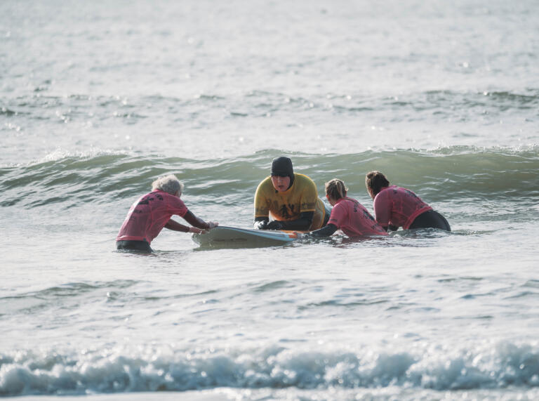 A man on a surfboard with a group of people helping. 
