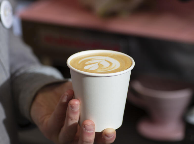 A hand holding a cup of milky coffee.