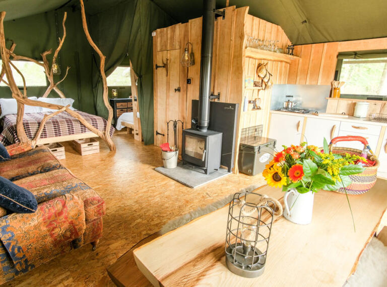 Inside a safari tent with log burner, bed, sofas and kitchen.