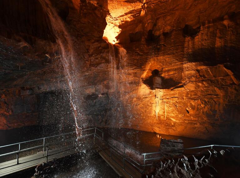 Water streaming down into a pool in an underground cave, lit up.
