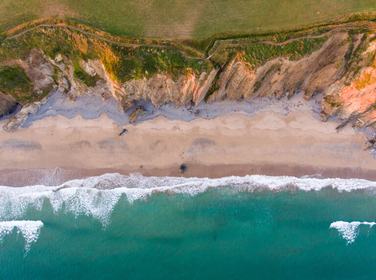 Luftaufnahme eines Strandes mit Klippen und Meer.