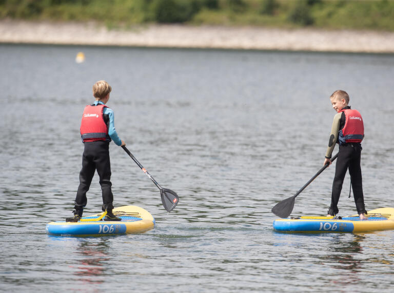 Two boys paddle boarding on the lake.