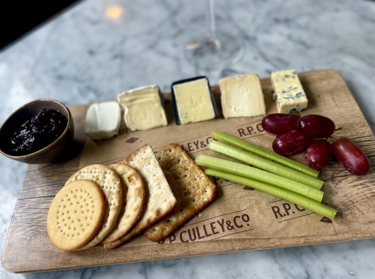 A selection of cheese with grapes, celery and crackers on a wooden board.