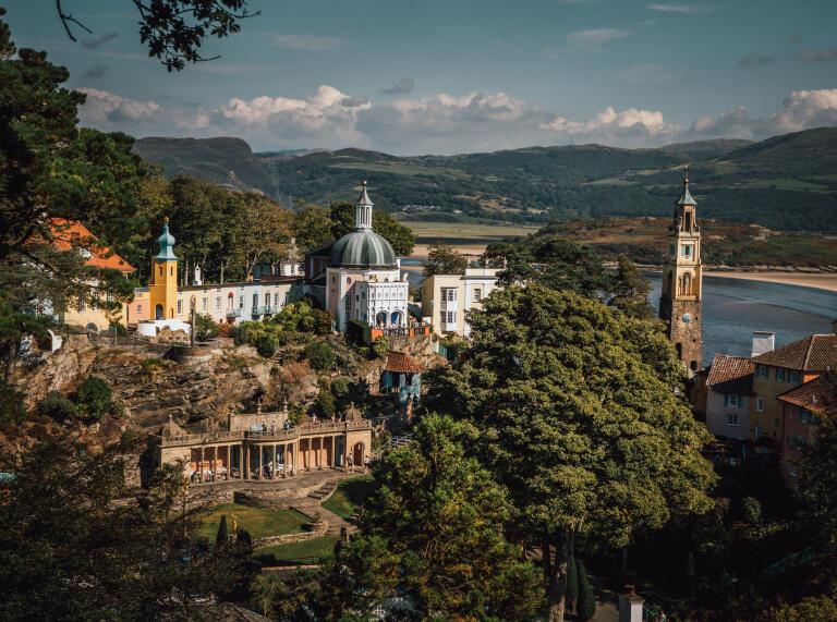 A view of the village of Portmeirion from above with the sea and mountains in the background.