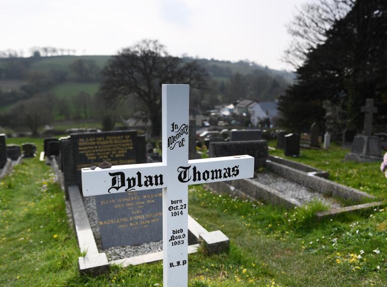 Grave with white wooden cross with Dylan Thomas on it.