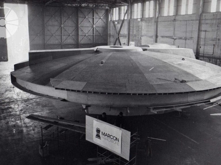 A black and white photo of a wooden spaceship for a film in a hanger.