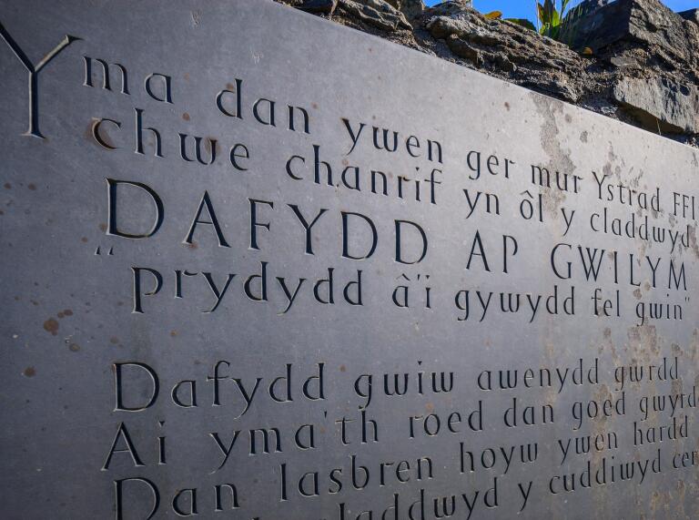 Geschnitztes Schild mit Angaben zum Grab von Dafydd Ap Gwilym in walisischer Sprache
