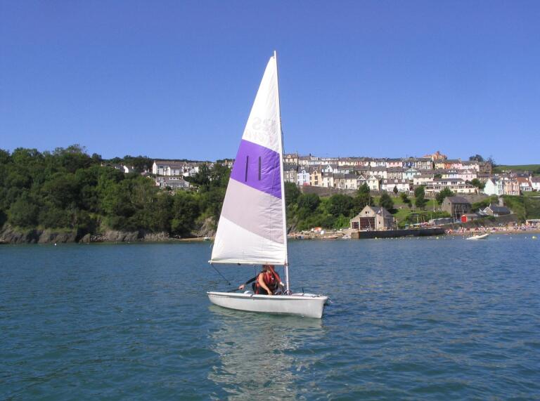 sailing boat on water, with coastal town in background.
