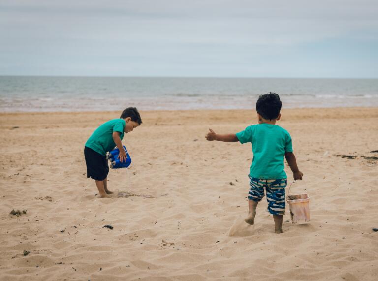 Two young children with buckets on a sandy beach.