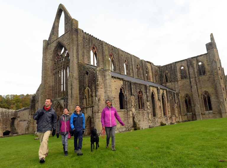 A group of people with a dog walking round a ruined abbey.