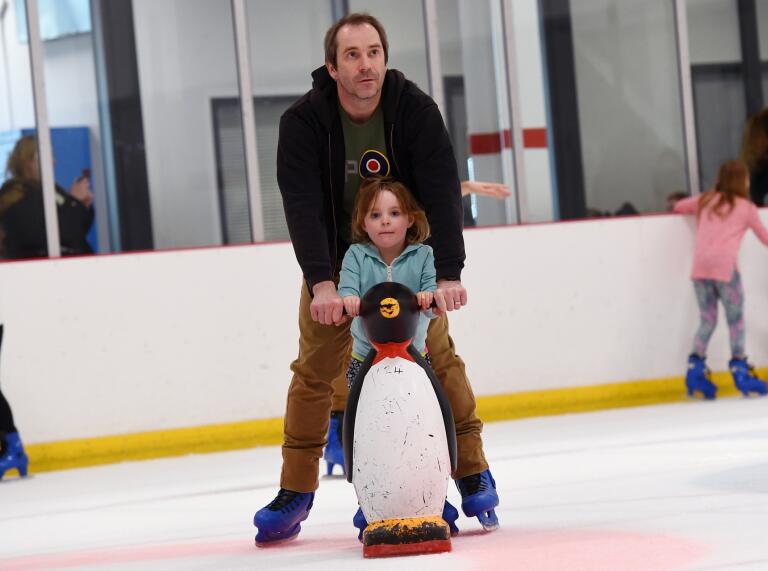 A man and a child skating on the ice holding one of the child supports.